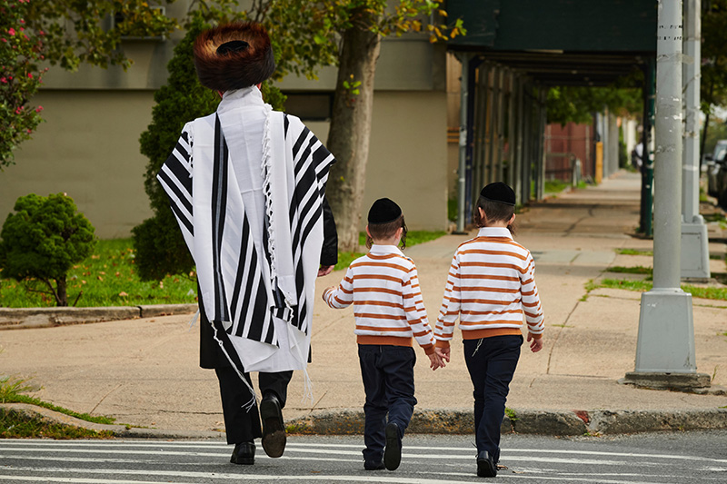 chassid in talis walking with his two young sons